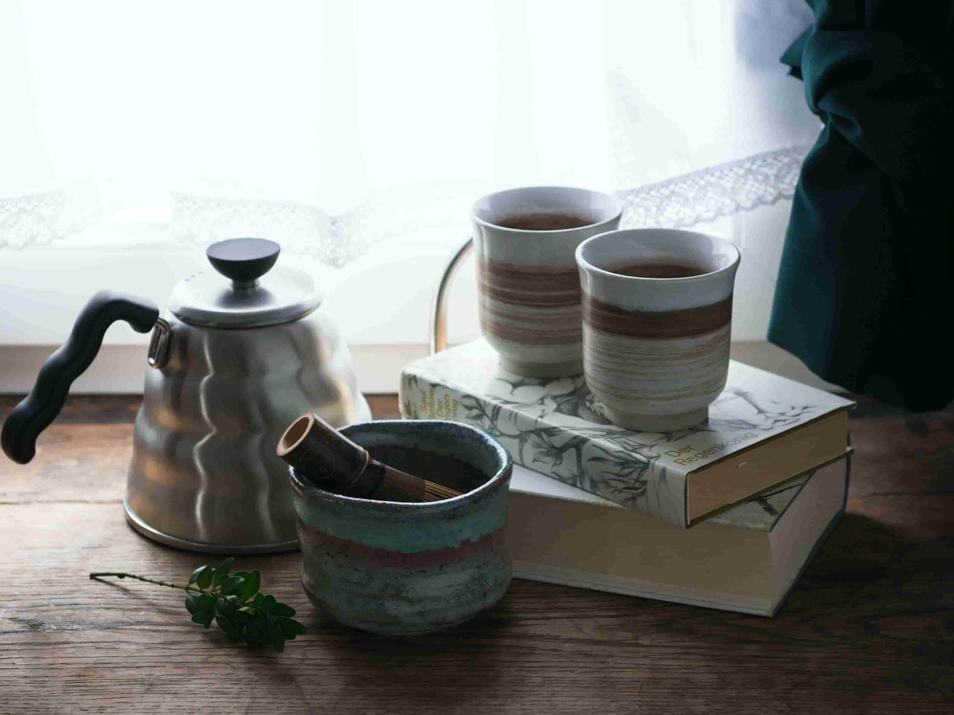 Matcha Schale, daneben Wasserkanne und zwei Becher auf Büchern