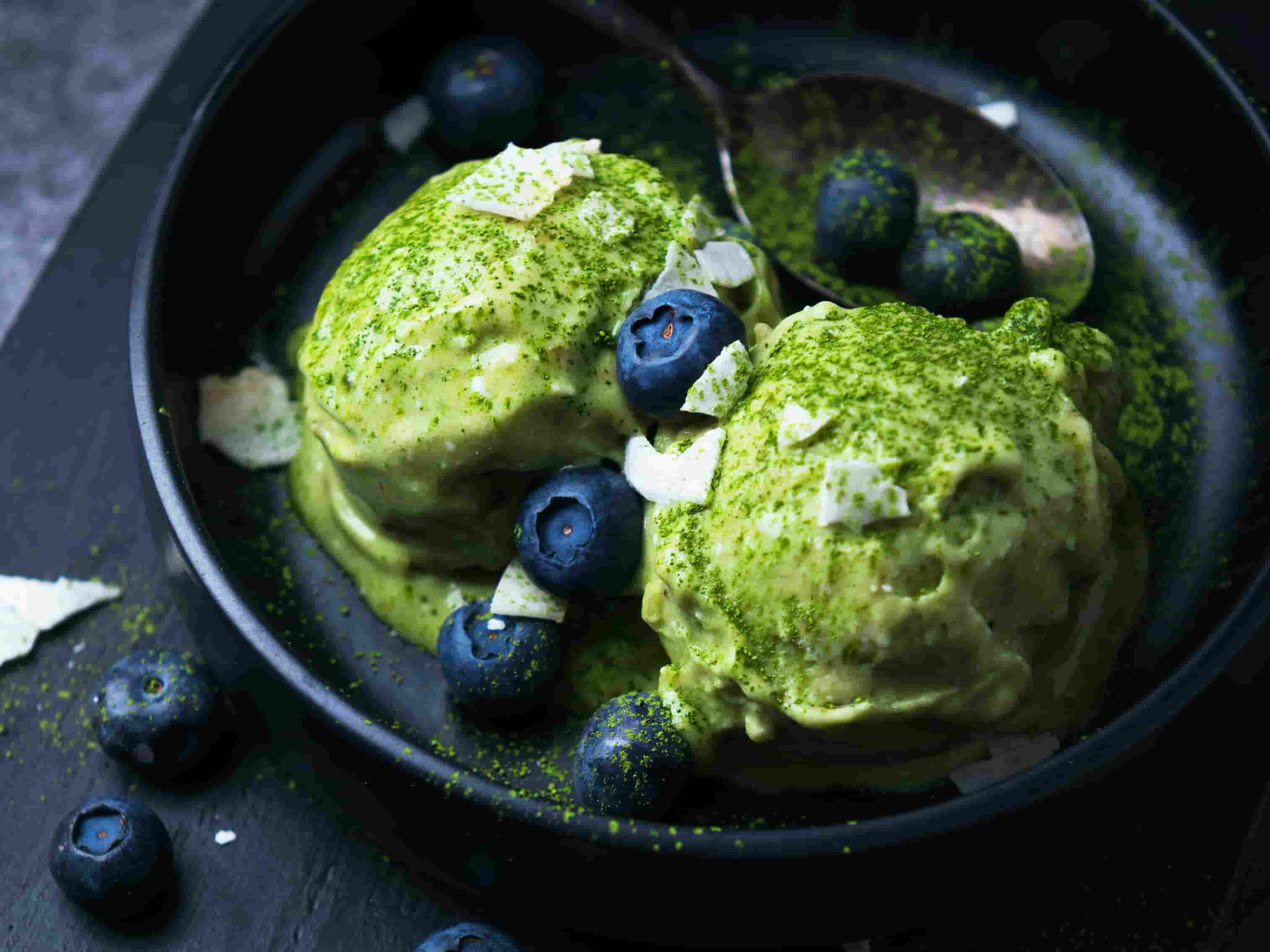 Gruenes Eis mit Blaubeeren und Kokosflocken in schwarzer Schale