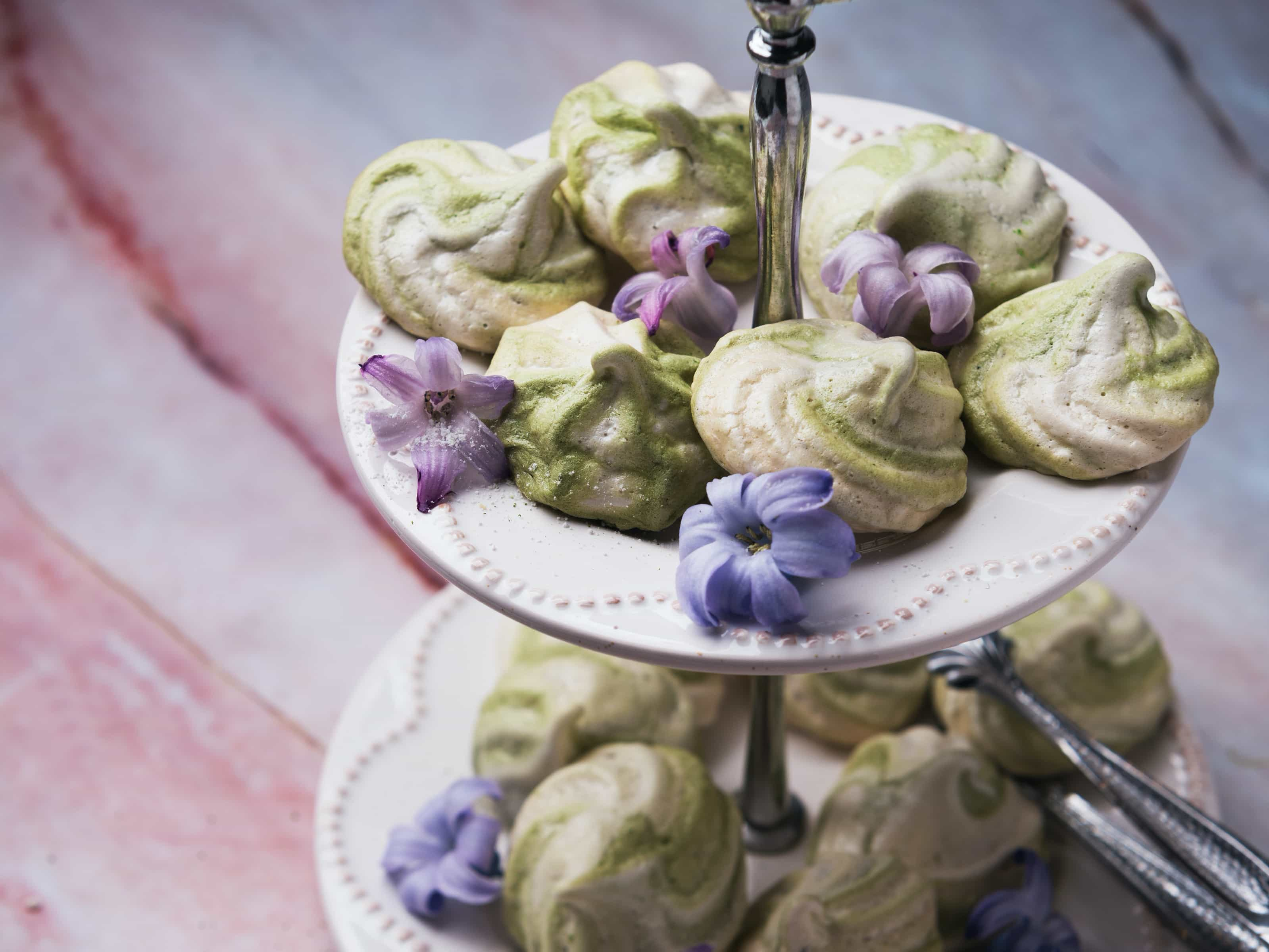 Matcha Meringues auf Etagere angerichtet mit rosafarbenen Blumen dazwischen