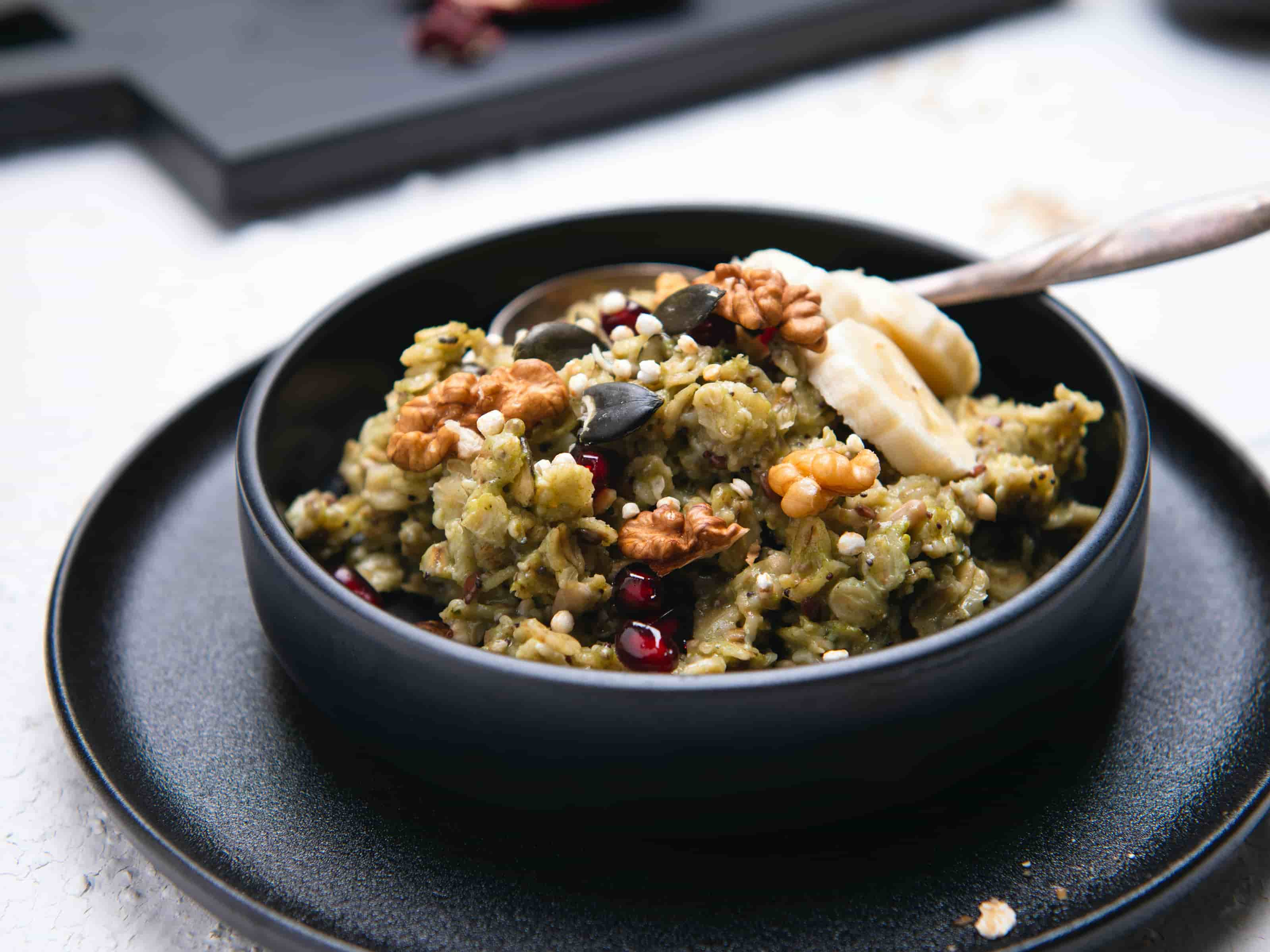 Gruenes Porridge in schwarzer Schale mit Nuessen und Bananen darauf