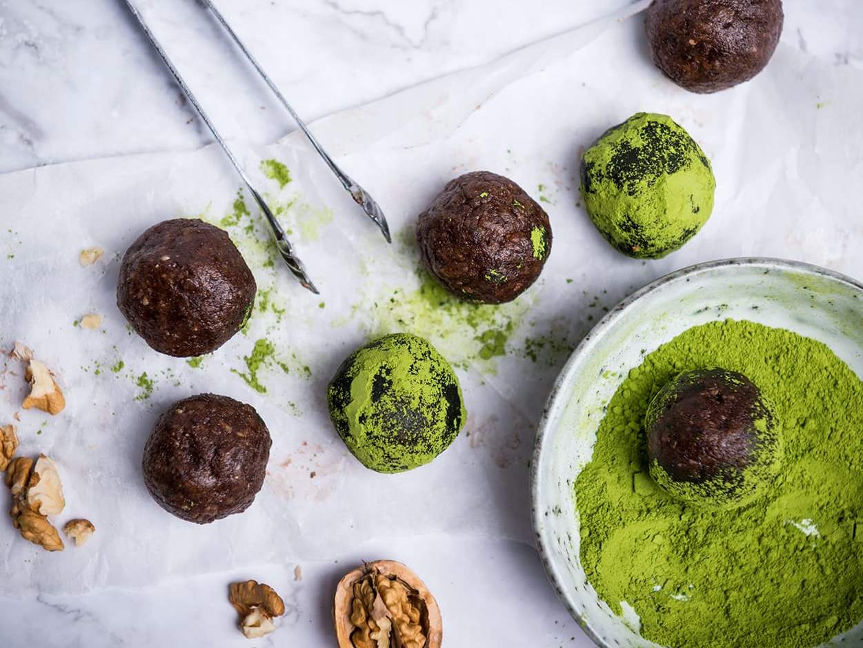 Braune Snack Kugeln auf Marmor Untergrund, teilweise mit Matcha bestaeubt 